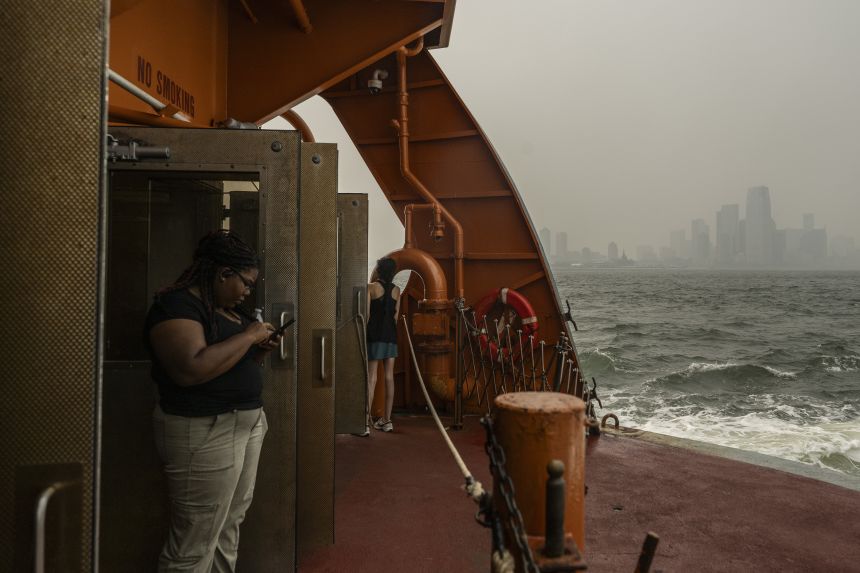 A woman look son from the deck of a Staten Island Ferry as the haze blankets the New Jersey skyline on Friday, July 16, in New York.