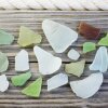 A close-up, high-angle photograph showing various colors of green, blue, white, and brown sea glass neatly arranged on a wooden surface.