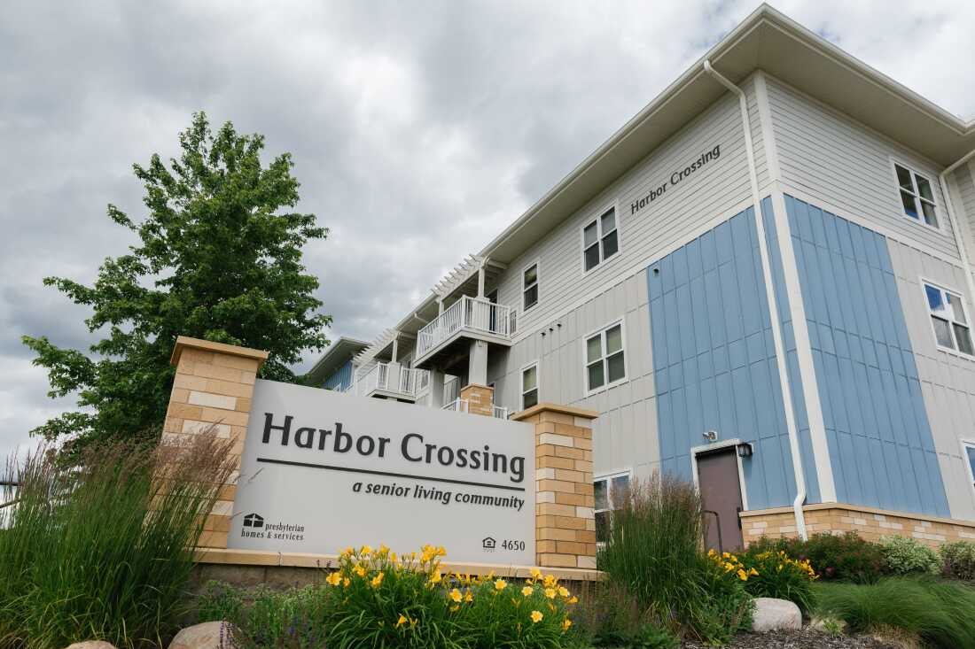Harbor Crossing in White Bear Lake, Minnesota, is photographed under a cloudy sky. It is a pleasant and new looking blue and gray building.