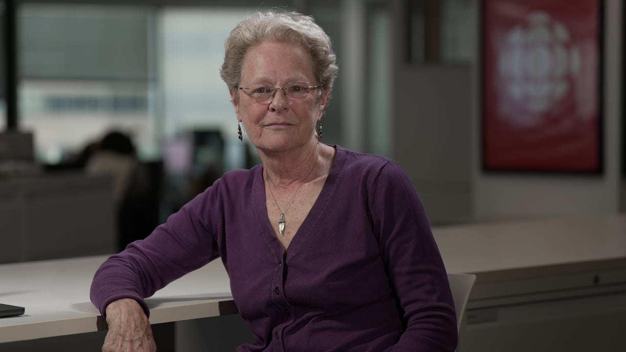 A woman poses for a photo, leaning against a desk
