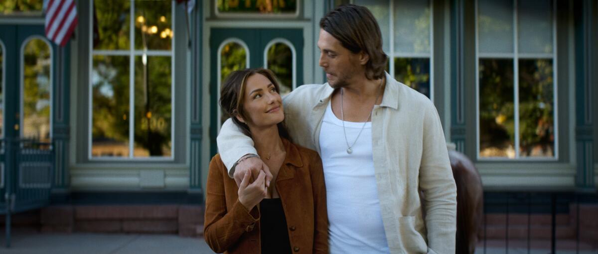 A man wraps his right arm around a woman while standing in front of a building