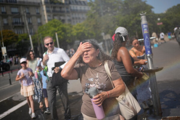 Tourists cool off at a public water fountain in Paris, June 26, 2026. (AP Photo/Christophe Ena, File)