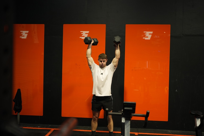 A man holds handheld weights in the air.