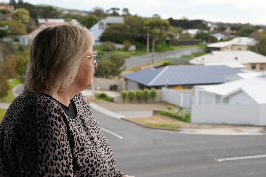 A woman looks out into her backyard. A hill slopes behind her.