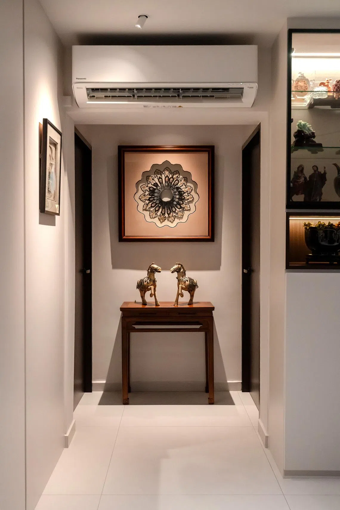 Between the bedroom doors are an antique side table, a pair of horse figurines and a framed yunjian (cloud collar).