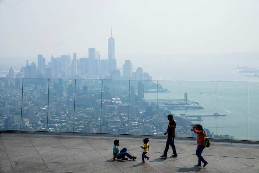 People visit the Edge observation deck as the New York skyline and One World Trade Center are seen through a cover of wildfire smoke on July 15, 2026.