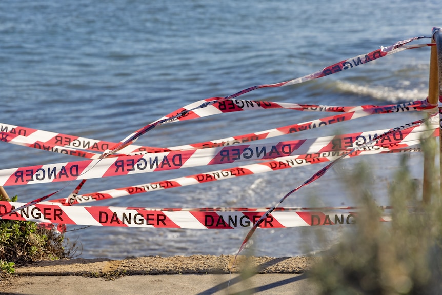 Red and white tape which says 'danger' in front of the ocean.