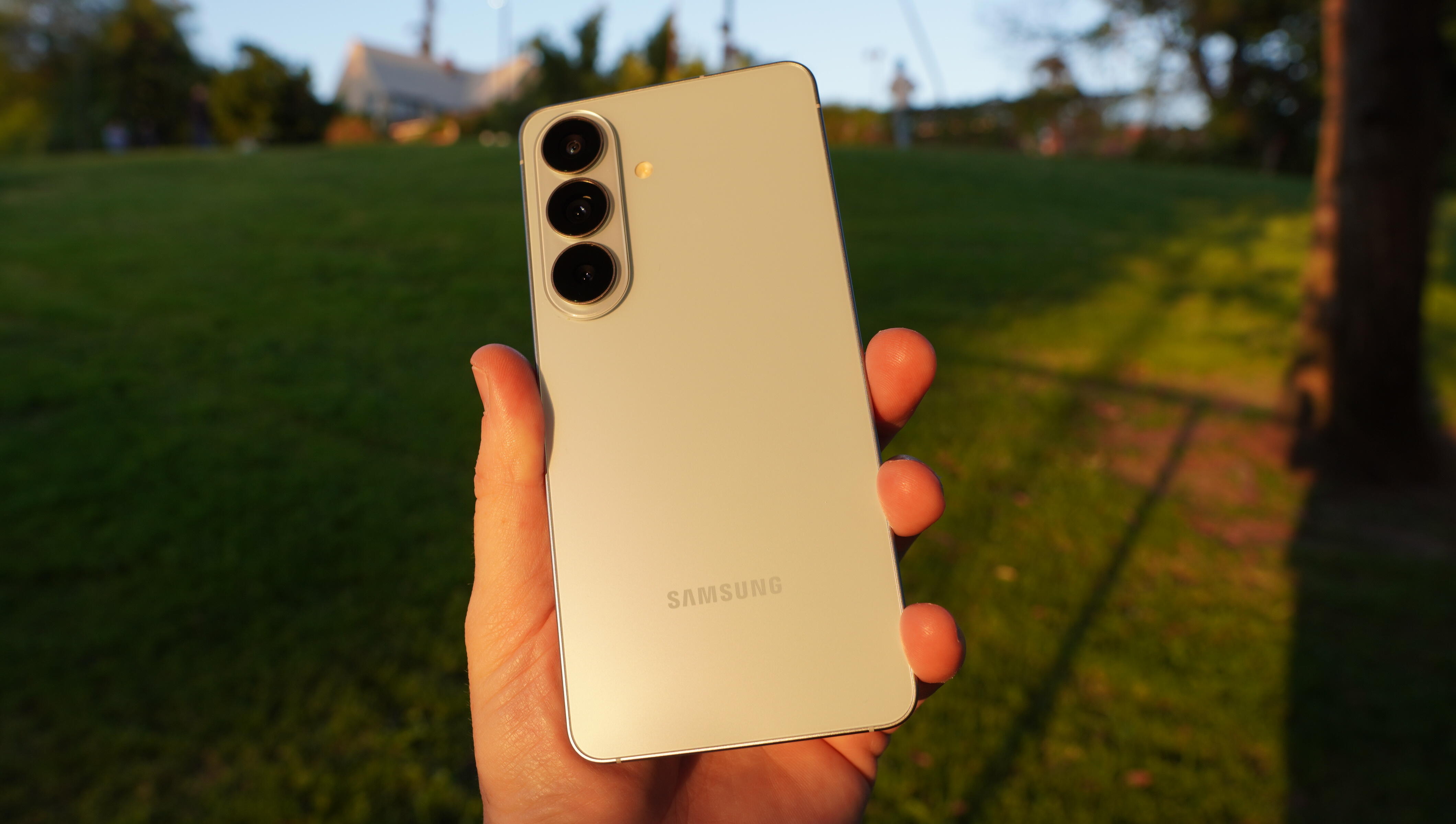A light blue phone held up at sunset in a park.
