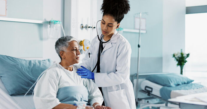 A compassionate doctor from the medical industry checks on an elderly patient in a hospital bed with a stethoscope.