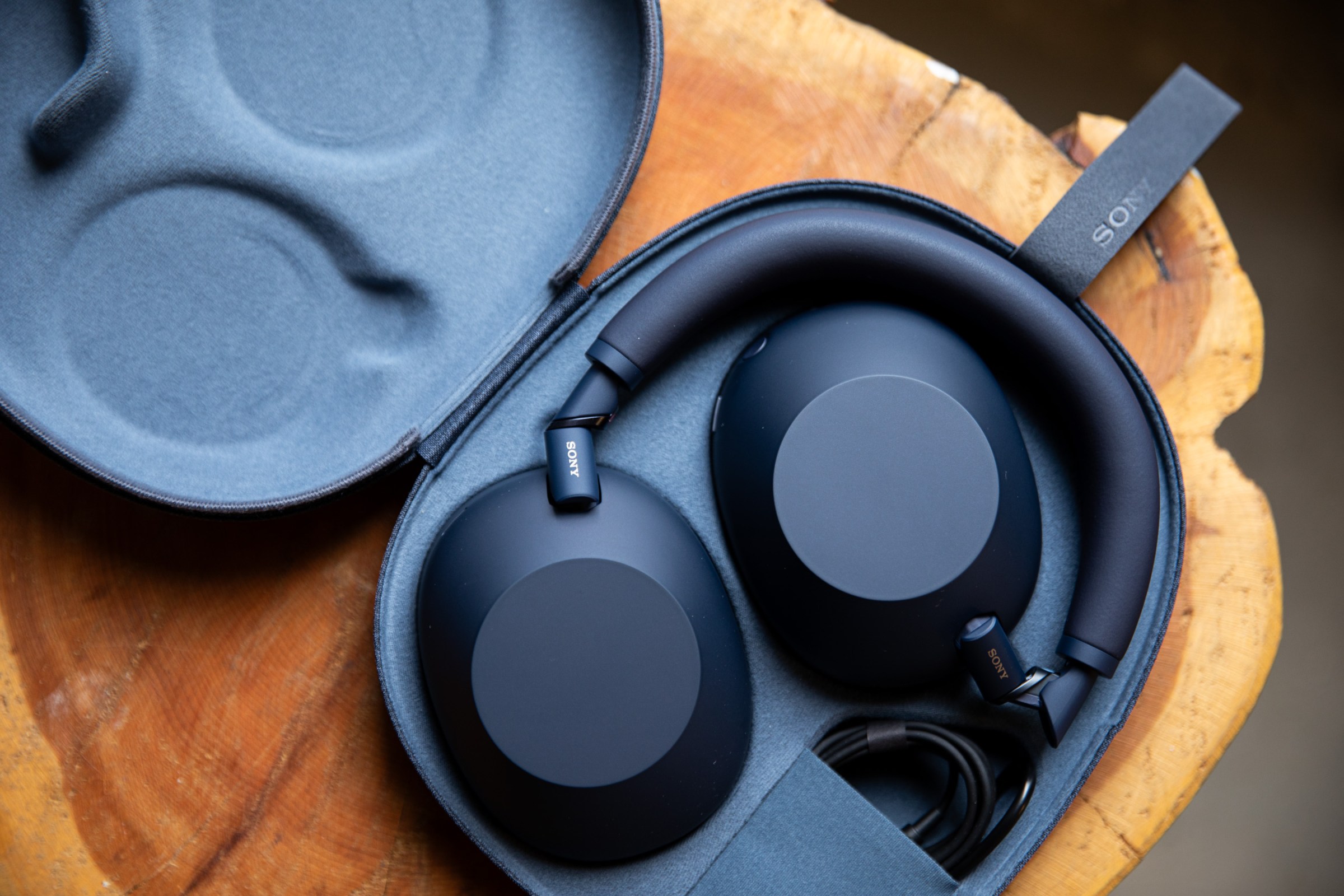 The Sony WH-1000XM6 wireless headphones in their carrying case atop a wooden table.
