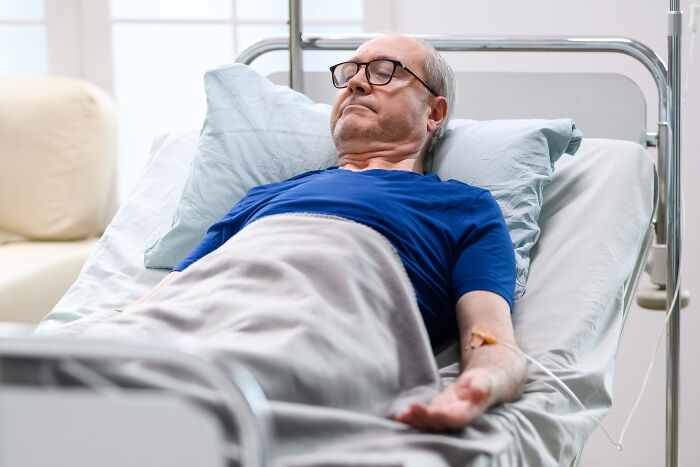 An elderly man with an IV in his arm lies in a hospital bed, illustrating truths about the medical industry.