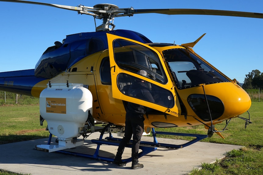 A brightly coloured helicopter on a small concrete pad, being loaded with fire ant bait
