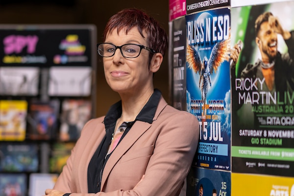 Samantha Bennett in a suit jacket leaning on a wall with posters of music artists on it 