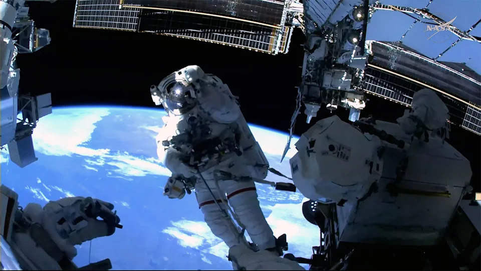 an astronaut in a full spacesuit is seen floating above Earth during a spacewalk outside of a space station