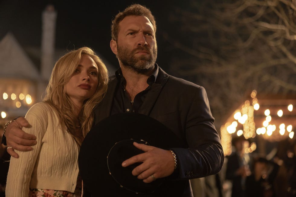 dutton ranch natalie alyn lind jai courtney couple embracing outdoors at night with lights in background.