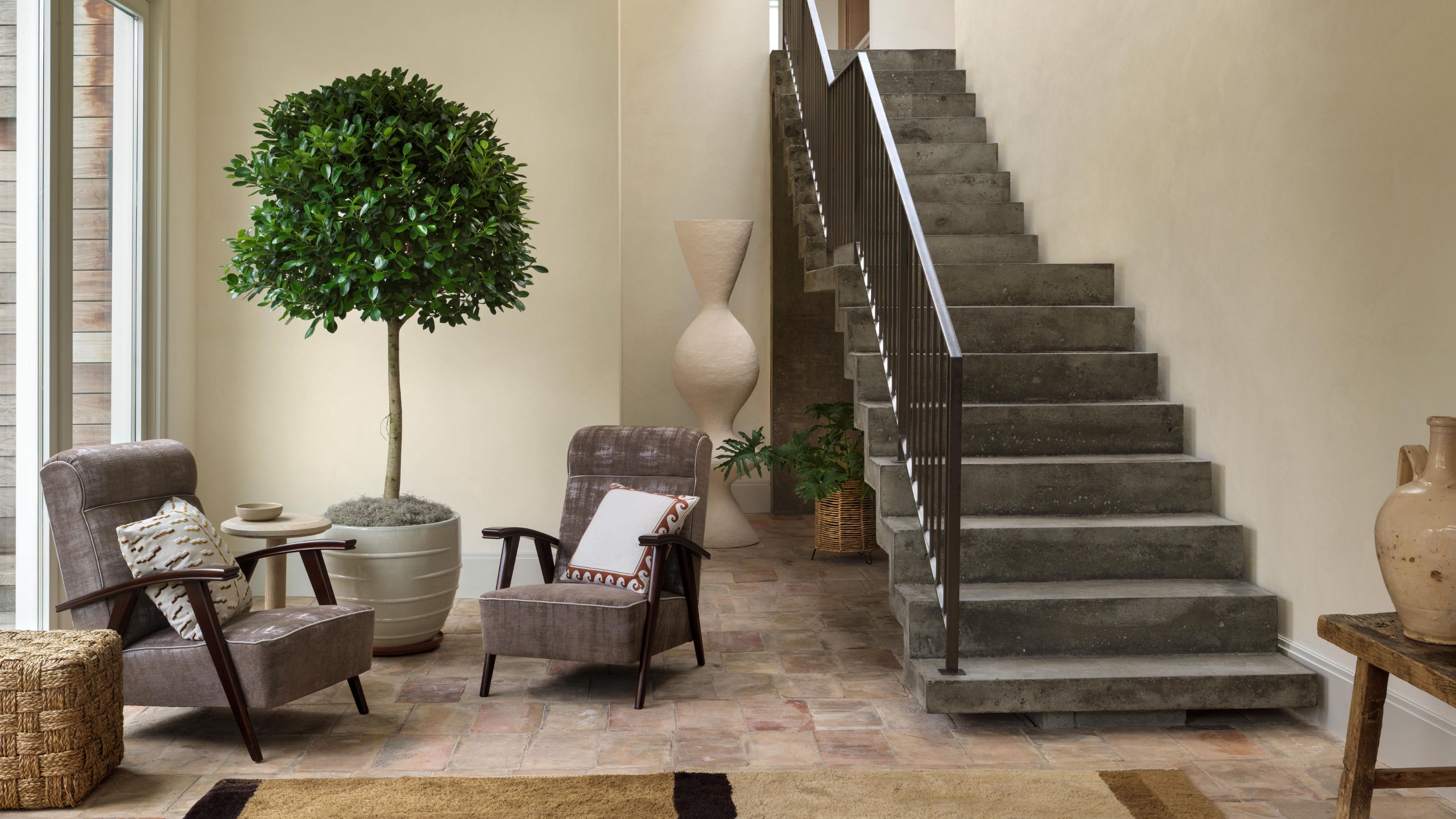 a large neutral poolhouse entryway with floating brutalist concrete stairs and terracotta floors