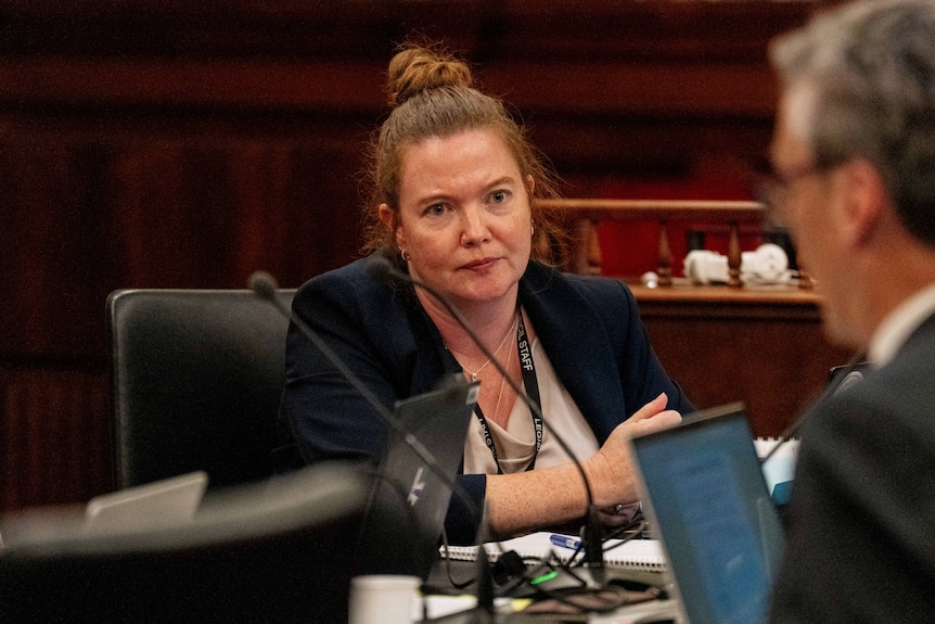 Woman looking sitting at a board room table looking at a man opposite her