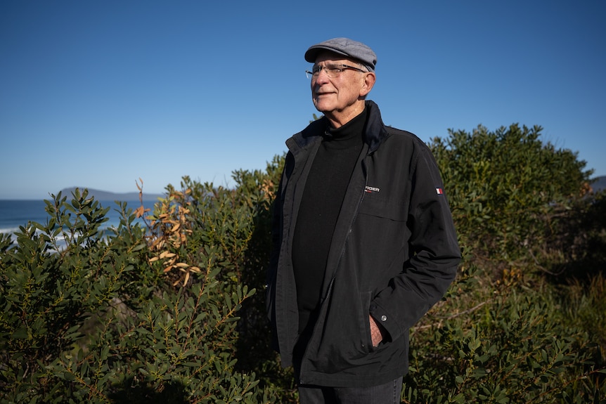 A man stands in front of bushland and ocean.