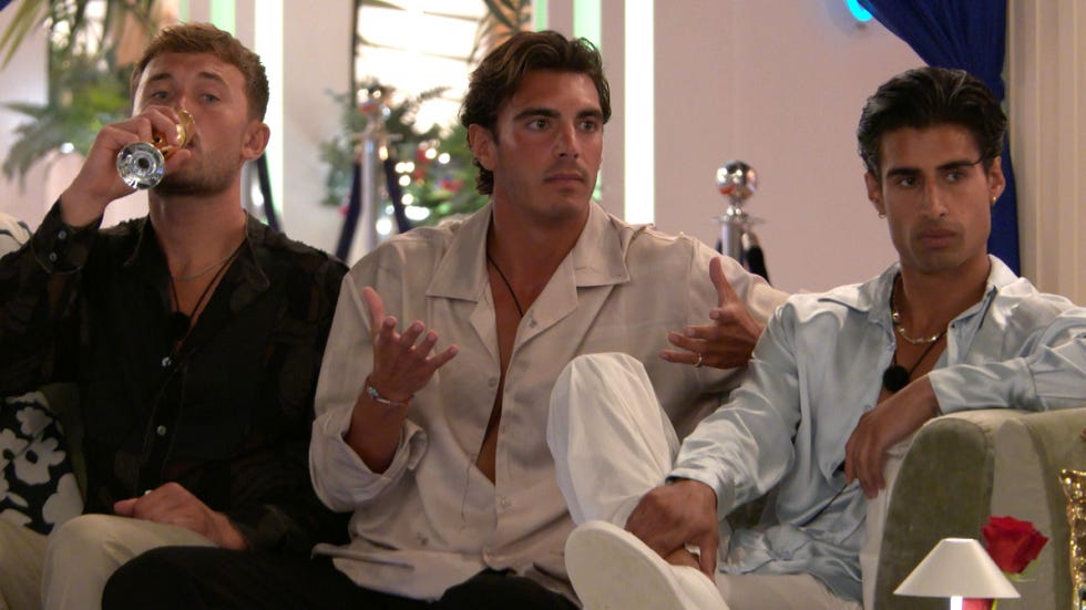 three men sitting on a couch, one drinking, one gesturing, and one looking serious.