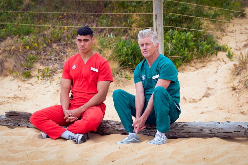 A TV still of Ioane Sa'ula, mid-20s, Samoan Australian, and Dan Wyllie, 56, sit together on a beach, looking sombre.