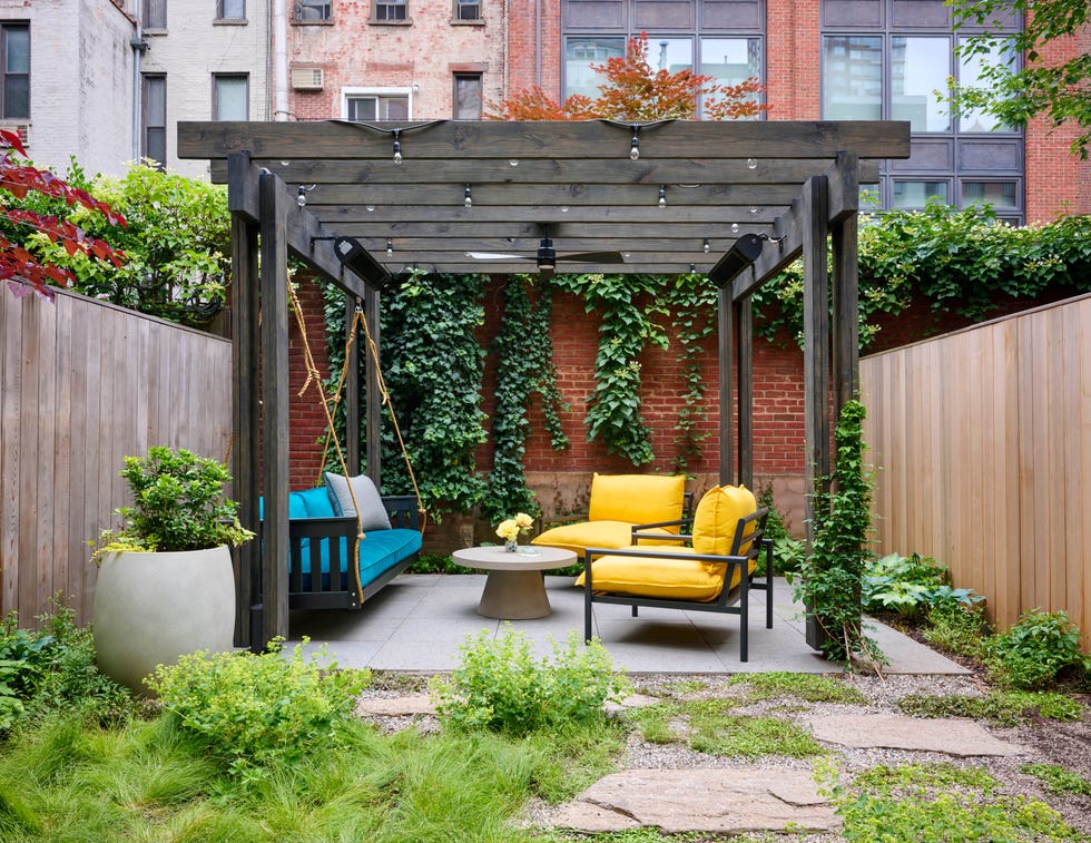 Cozy outdoor seating area with a swing and colorful furniture surrounded by greenery and wooden fencing.