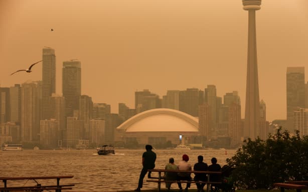 People look toward the downtown skyline from the Toronto Islands as forest fires in Northern Ontario cause poor air quality over the city, in Toronto, Ontario, Canada, July 15, 2026. Toronto had the worst air quality of any major city in the world on Wednesday, the Swiss firm IQAir said, as Canadian authorities urged people to stay indoors. Toronto edged out New Delhi and the Democratic Republic of Congo's capital Kinshasa as wildfire smoke turned the skies a hazy yellowish-grey in Canada's largest city. (Photo by Cole BURSTON / AFP)