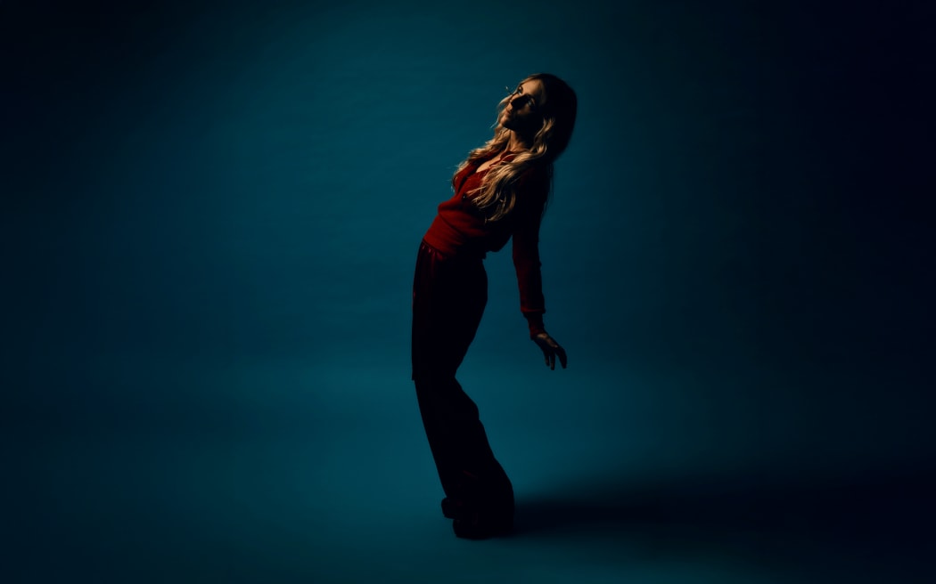Agnes Obel stands looking skyward in front of a deep blue background