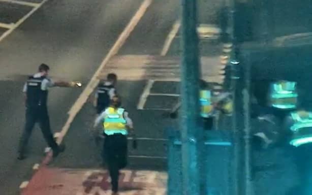 Caleb Turner stands in a T shape as police walk towards him before tasering him, as a group of Public Safety Officers sprint up the road.