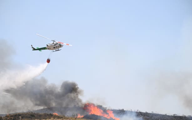 A picture taken on July 10, 2026 shows a helicopter dropping water in the area of a wildfire that killed 11 near Los Gallardos, in Almeria Province. Eleven people were killed and 19 are missing after a wildfire in Bedar, in Los Gallardos district, with four victims who may have been British who were burned in their car, authorities said. (Photo by JOSE JORDAN / AFP)