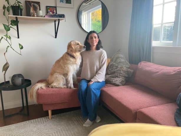 Amy McDaid and her golden retriever Isla sit on a large pink couch in a living room.