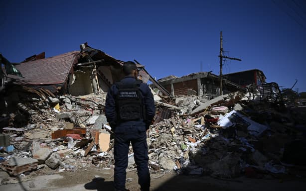 A Venezuelan national police officer of the Criminal Gang Unit stands guard next to rubble in El Junquito, Venezuela on June 29, 2026, after twin earthquakes. Hopes were fading on June 29, 2026 of finding survivors more than four days after powerful twin earthquakes struck Venezuela, as residents grow increasingly frustrated with the government's response to the disaster that has killed at least 1,450 people and left tens of thousands unaccounted for. (Photo by Federico PARRA / AFP)