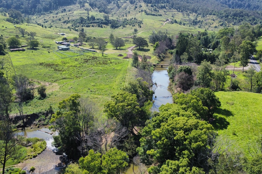 A wide drone shot of a green farm with brown creek winding through the property