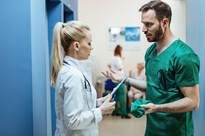 Two medical professionals, a doctor and a nurse, discussing medical industry issues in a hospital hallway.