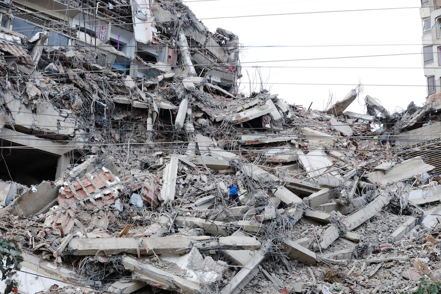 A man walks among the rubble of a building that collapsed in earthquakes.