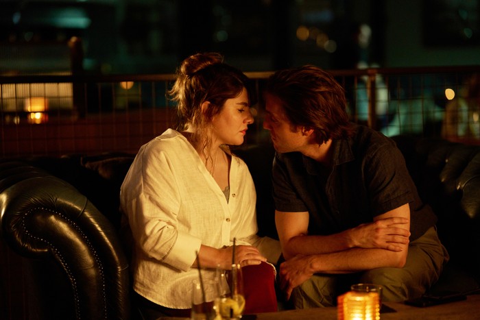 570517 Ruth Madeley as Dr Gabriele Fox and Jack Farthing as Frasier Melville in The Rapture, sat together, leaning in to kiss.