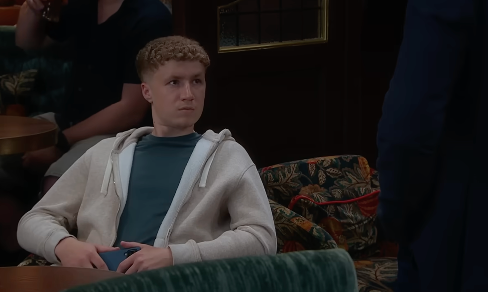 person sitting on a patterned sofa, looking to the side, in a room with a wooden table and dark background. person sitting on a patterned sofa, looking to the side, in a room with a wooden table and dark background.