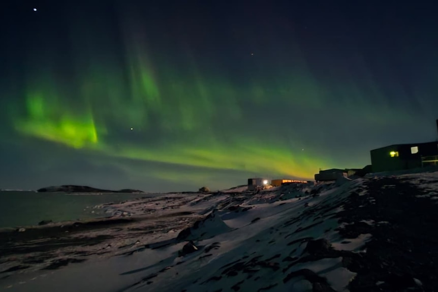 A night photo of an aurora with green lights in the sky