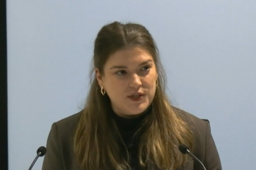 A brunette woman with her hair tied half up half down wearing gold earrings.