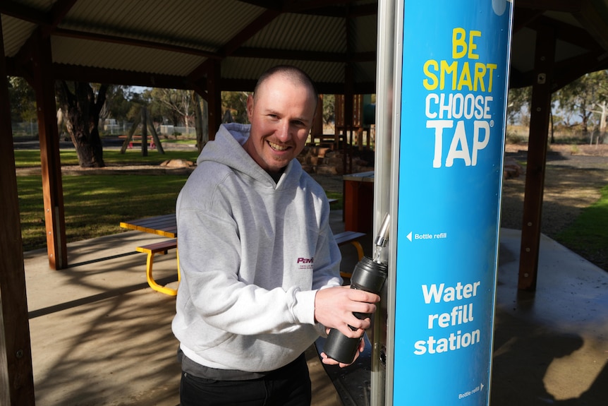 Man holding drink bottle under tap.