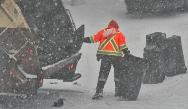 A garbage man empties cans of garbage into a garbage truck as a snowstorm hits Toronto on December 26, 2025.