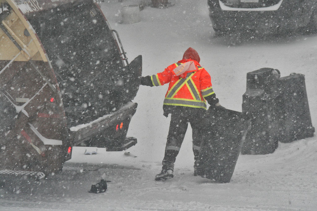 A garbage man empties cans of garbage into a garbage truck as a snowstorm hits Toronto on December 26, 2025.