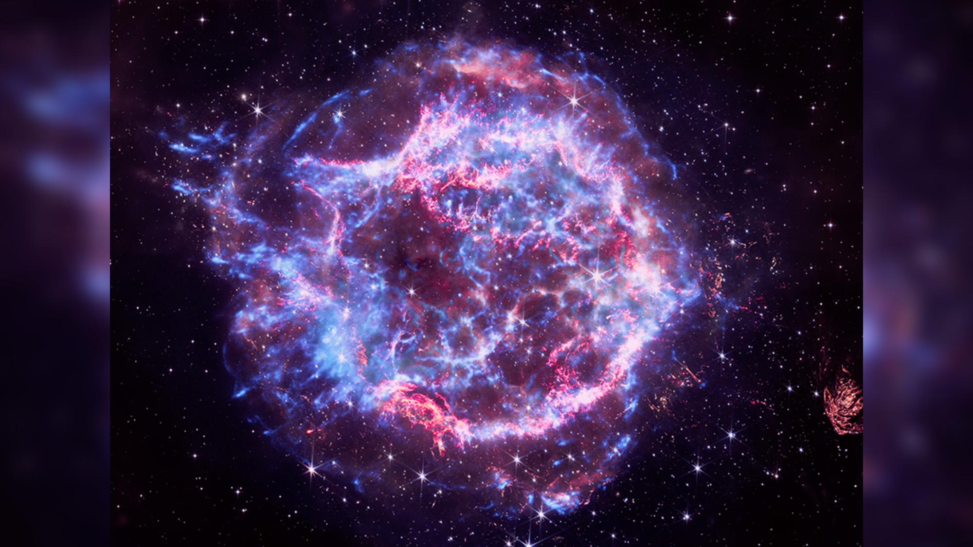 a swirl of blue-and-purple gases amid red pinpoints of light, on a black background