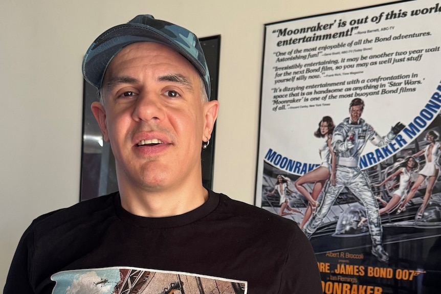 Man in black t-shirt stands in front of James Bone movie poster.