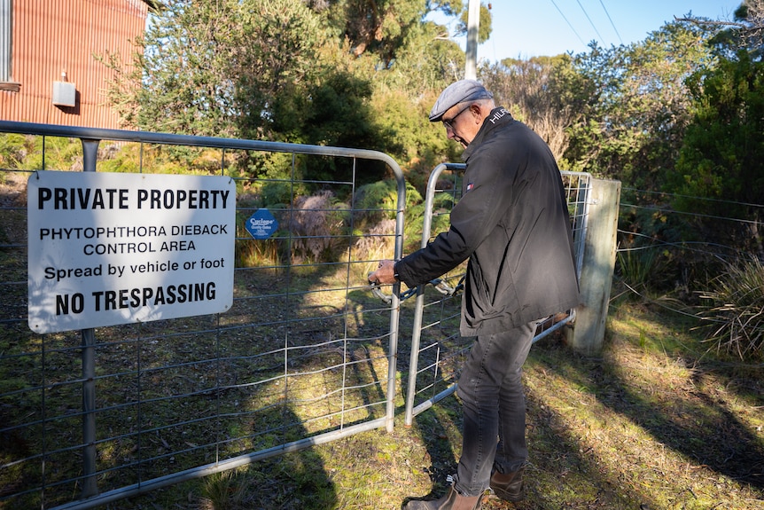A man unlocking the gates to a private property, with bush and a shed in the background.