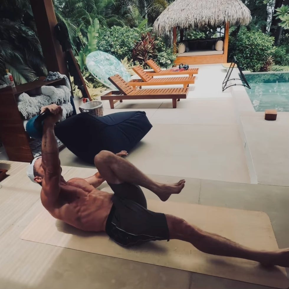 man exercising with kettlebell on a patio next to a pool. man exercising with kettlebell on a patio next to a pool.