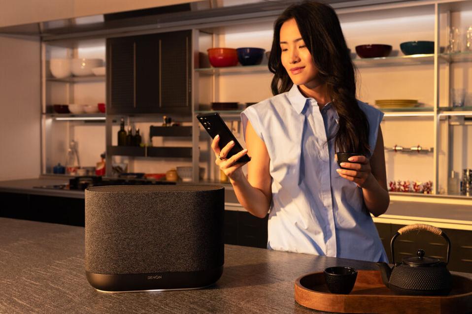 A woman using a remote to operate the Denon Home 400 speaker in a modern kitchen