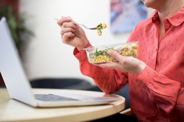Stock image of a woman eating her lunch at her desk at work