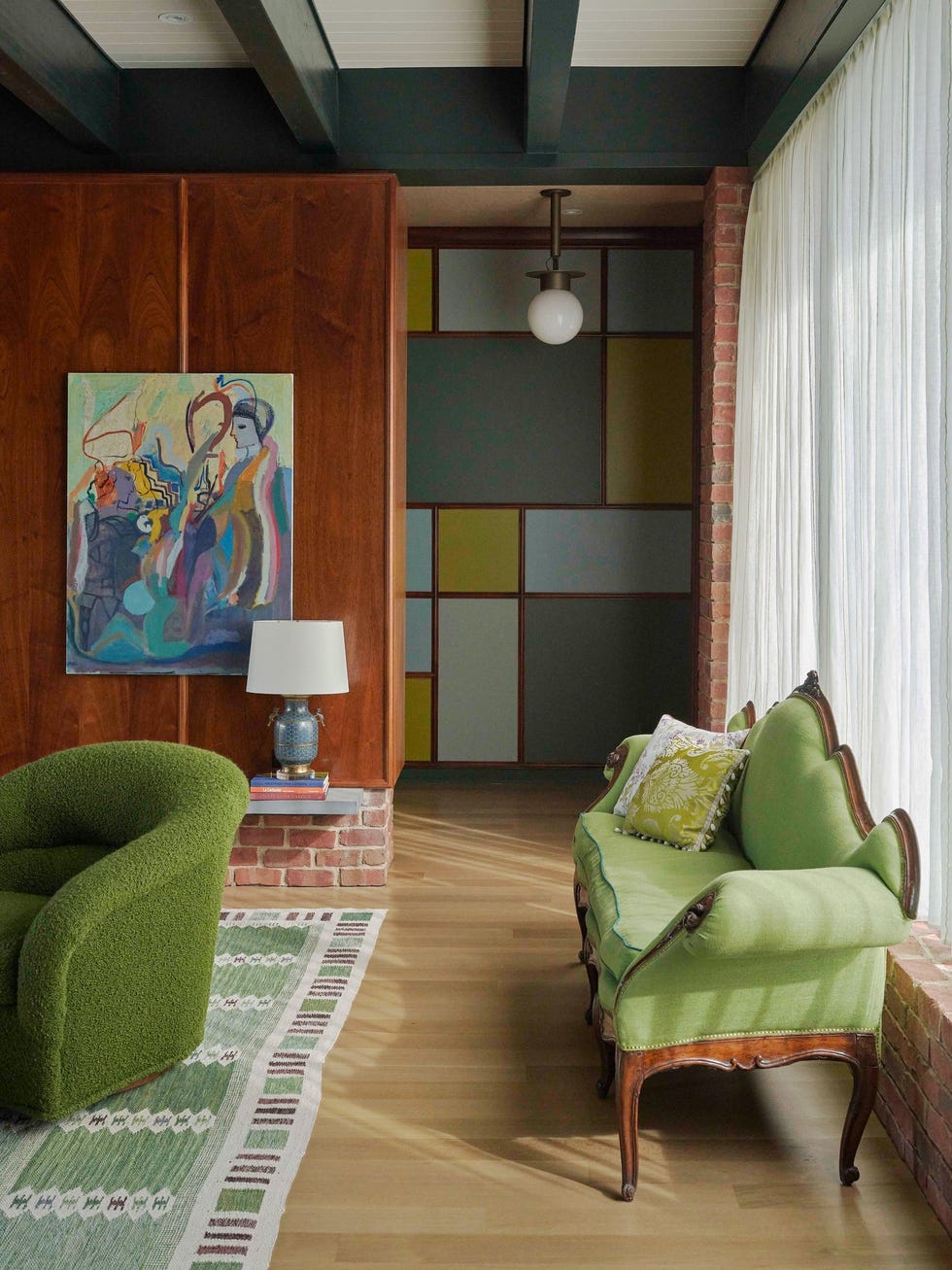 Cozy living room with green furniture, art on wall, and large window with light drapery.