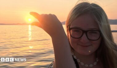 Lucy is wearing glasses and a necklace, posing as if she is trying to pinch the sun at sunset