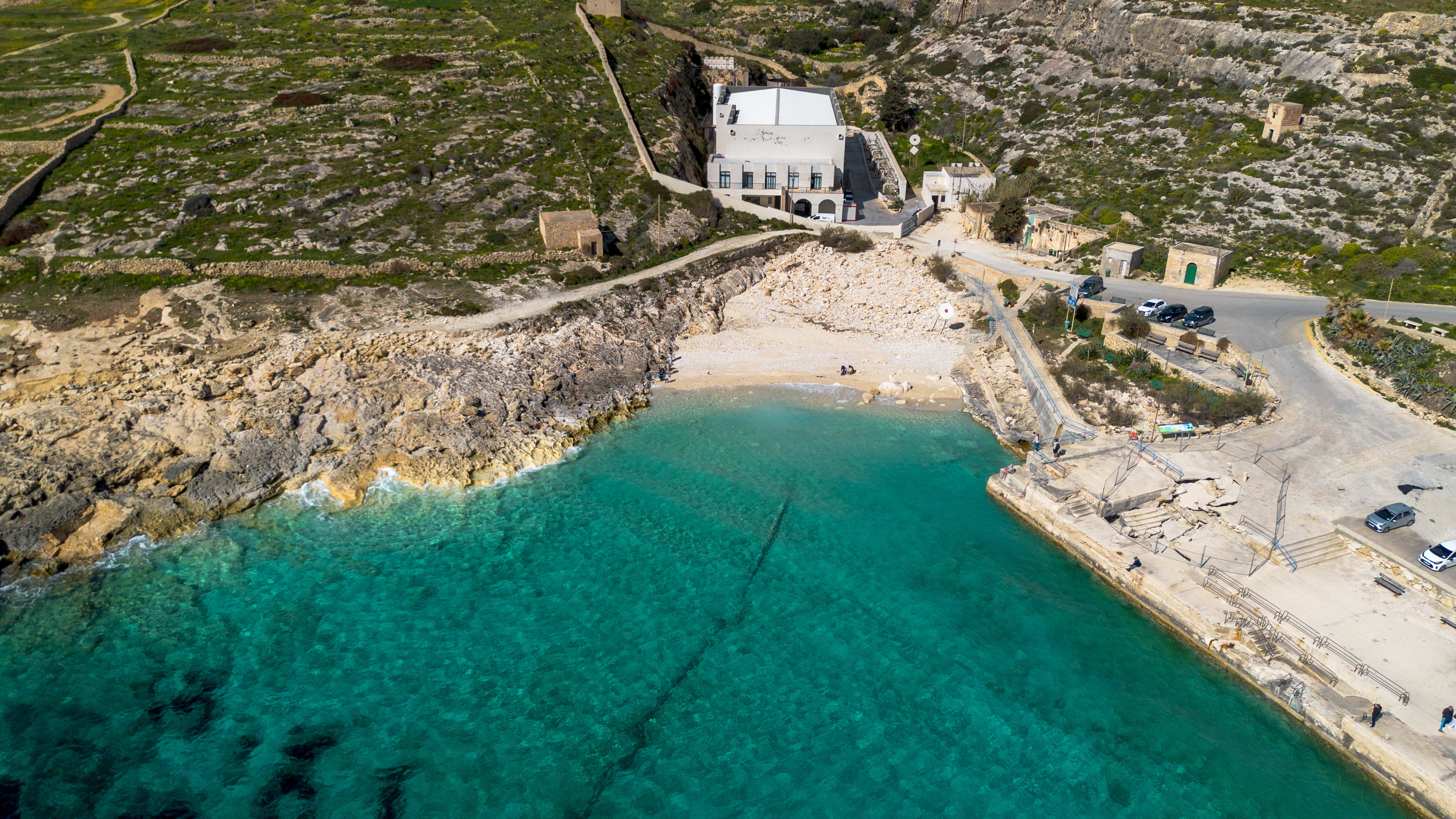 Aerial view of the Hondoq ir Rummien ir-rummein desalination plant, rocky shoreline, small beach and offshore brine outfall pipe visible in the turquoise Mediterranean water in Qala, Gozo, Malta
